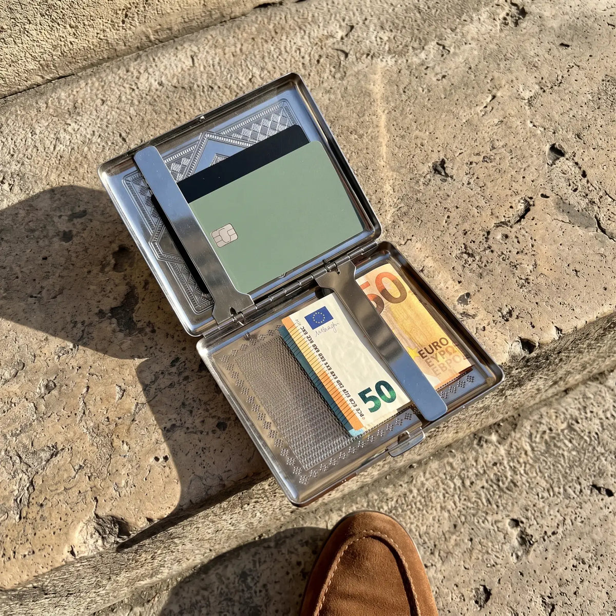 Étui N°2 Losange ouvert avec des cartes et des billets, posé sur des marches en pierre